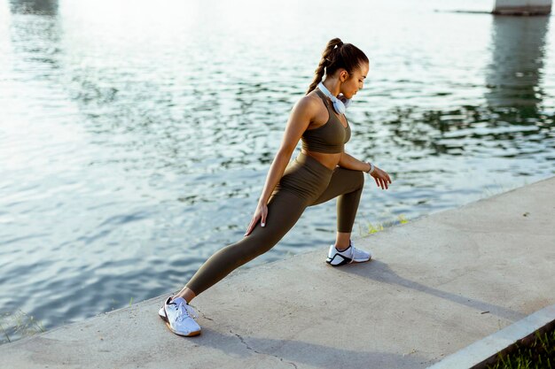 Young woman in sportswear stretching on a river promenade