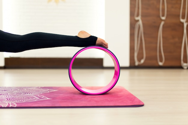 Young woman in a sportswear yoga exercises with a yoga wheel in the gym