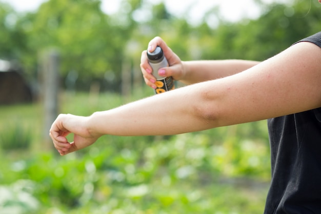 Giovane donna che spruzza repellente per insetti per zanzare nella foresta