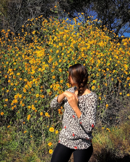 Foto giovane donna in piedi contro i fiori gialli al parco