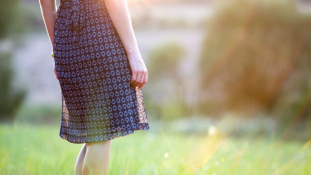 暖かい夕日を楽しんでいる緑の芝生のフィールドに一人で立っている若い女性。