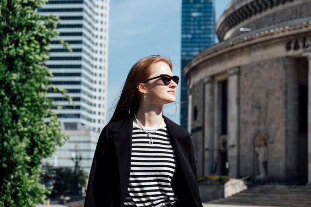 Photo young woman standing alone looking at the modern downtown high-rises skyscrapers street city view