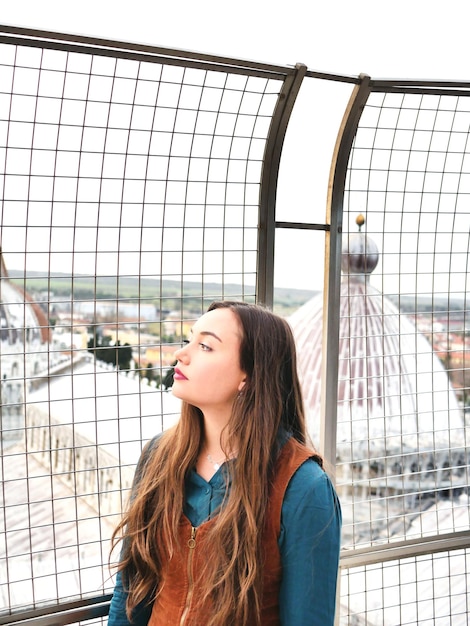 Photo young woman standing by fence in city