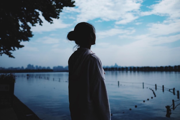young woman standing by lake against sky