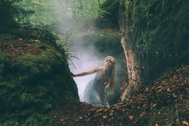 Foto giovane donna in piedi vicino a una roccia nella foresta