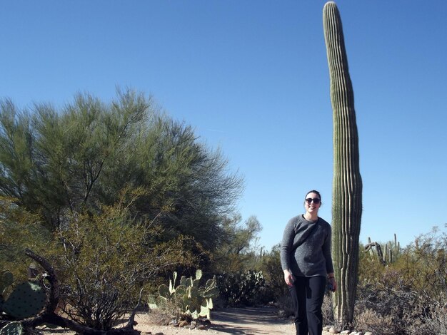 Foto giovane donna in piedi vicino al cactus saguaro sul campo contro un cielo blu limpido