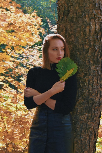 Young woman standing by tree trunk during autumn