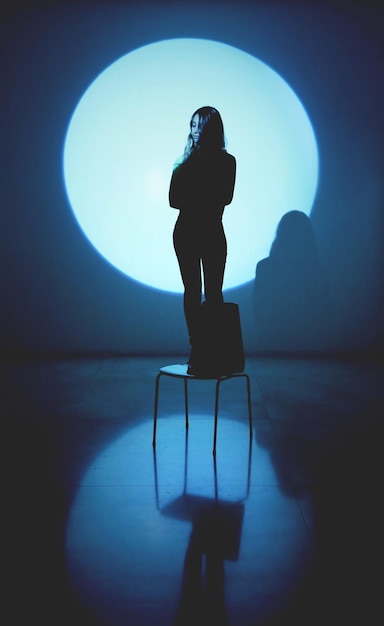 young woman standing on chair against spotlight