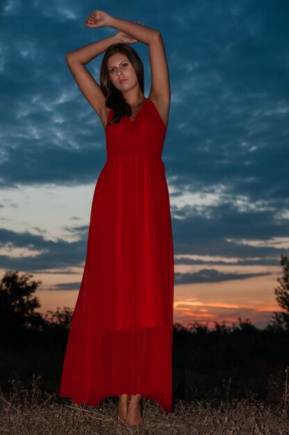 Photo young woman standing on field against sky during sunset