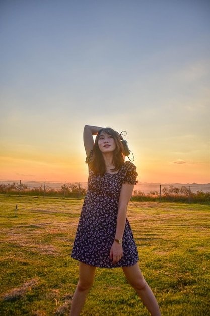 Young woman standing on field against sky during sunset