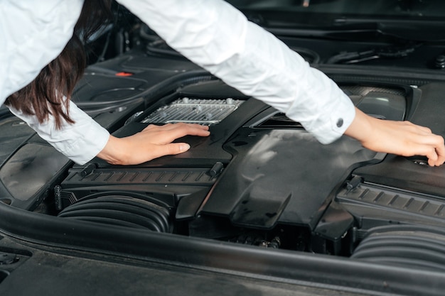 車のボンネットの下を見て開いたフードで車の前に立っている若い女性