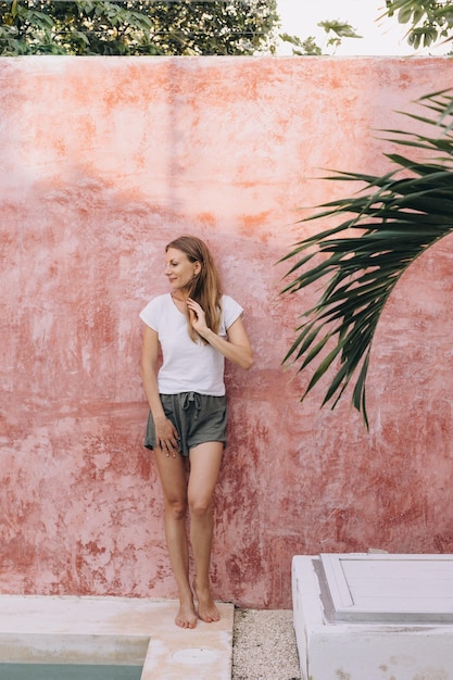 Young woman standing in front of a coral coloured wall touching her hair in tulum mexico