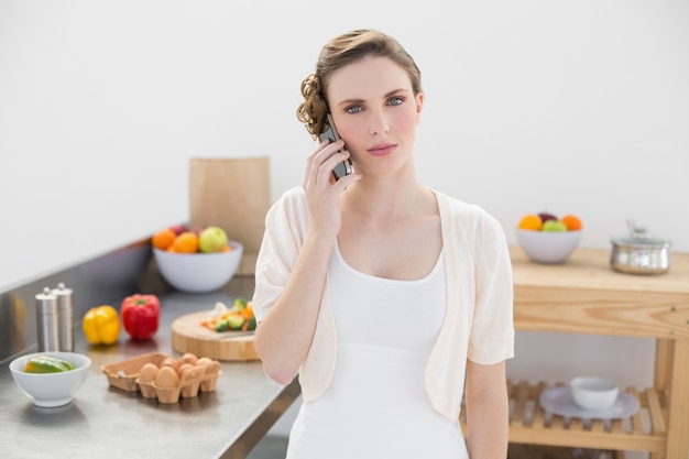 Young woman standing in kitchen while phoning 