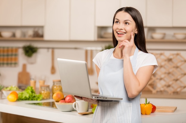 ノートパソコンとキッチンに立っている若い女性