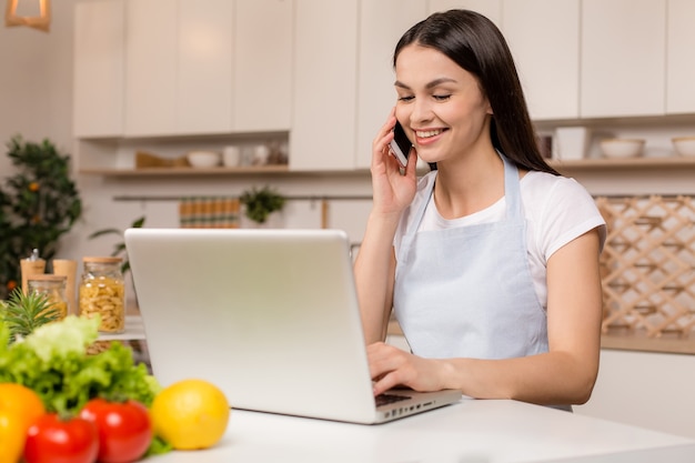 Young woman standing in the kitchen with laptop