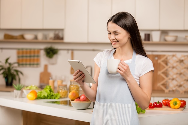 タブレットでキッチンに立っている若い女性