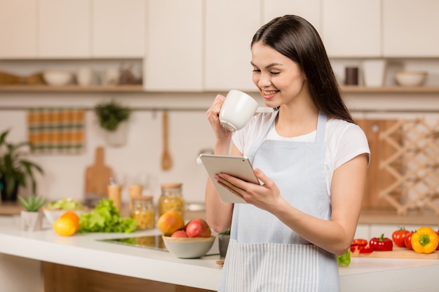 タブレットでキッチンに立っている若い女性