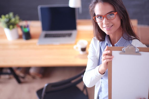 Young woman standing near desk with laptop holding folder and cup of coffee Workplace Business Woman