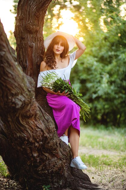 Young woman standing near the old tree looking at camera and smiling feeling good outdoors