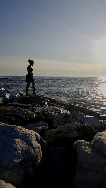 写真 夕暮れの空に向かって海のそばの岩の上に立っている若い女性