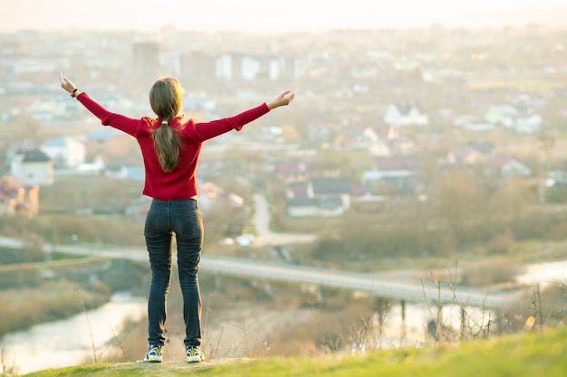 Young woman standing outdoors raising her hands enjoying city view. Relaxing, freedom and wellness concept.