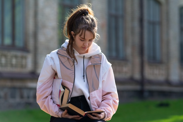 Young woman standing reading a book outdoors