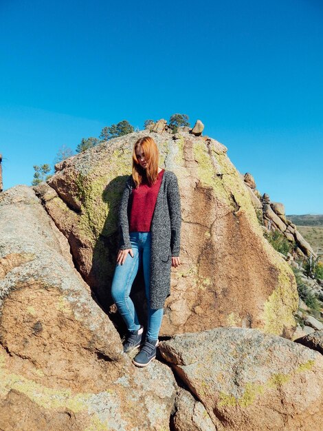 Young woman standing on rock against blue sky