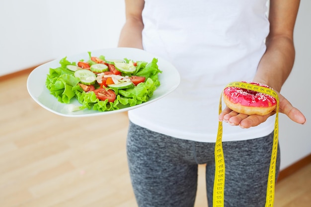 Young woman standing on scales and holding a donut and salad