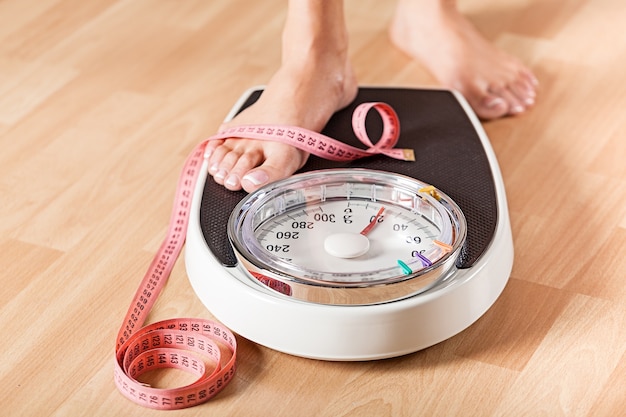 Young woman standing on scales with measuring tape on wooden background