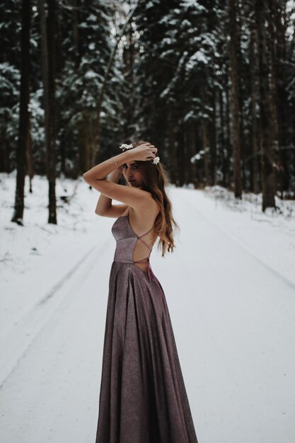 Photo young woman standing on snow covered land in a prom dress