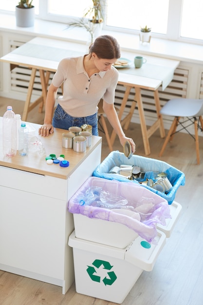 Young woman standing at the table in the kitchen and segregating waste to correct containers