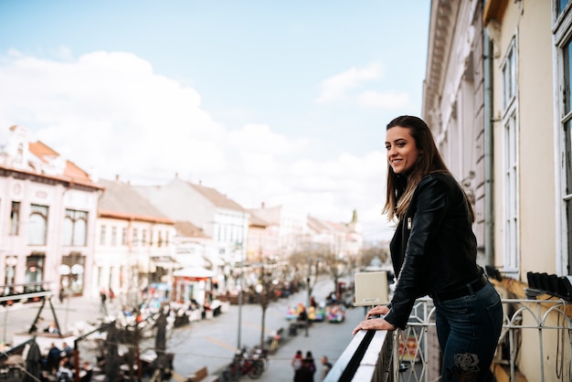 Молодая женщина, стоя на террасе над улицей города.