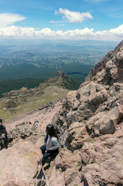 Young woman standing on top of cliff in summer mountains