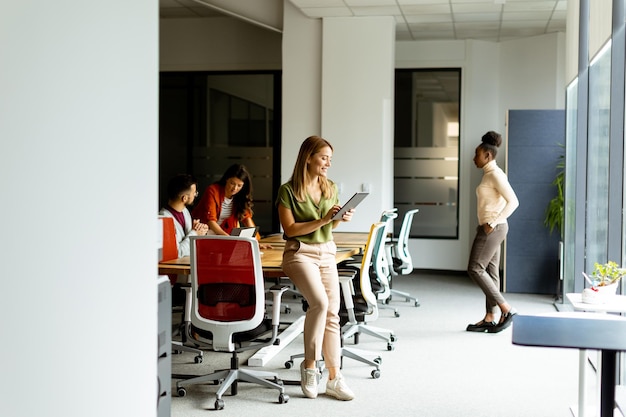 Young woman standing with digital tablet in front of her team at the modern office