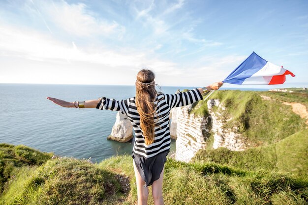 Foto giovane donna in piedi con bandiera francese sulla sommità della costa rocciosa sopra l'oceano vicino alla città di etretat in france