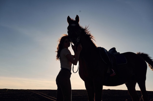 晴れた日中に農業分野で彼女の馬と一緒に立っている若い女性