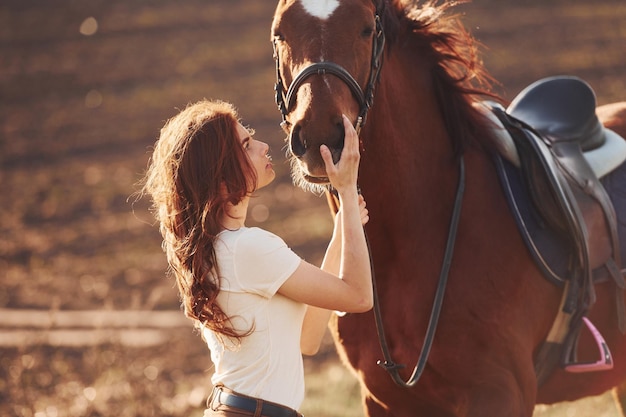 晴れた日中に農業分野で彼女の馬と一緒に立っている若い女性