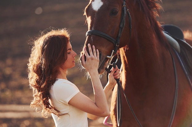晴れた日中に農業分野で彼女の馬と一緒に立っている若い女性
