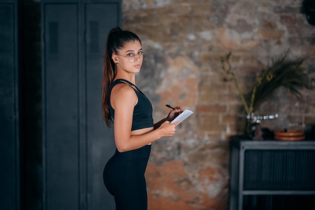 Young woman standing writing down something into the notebook