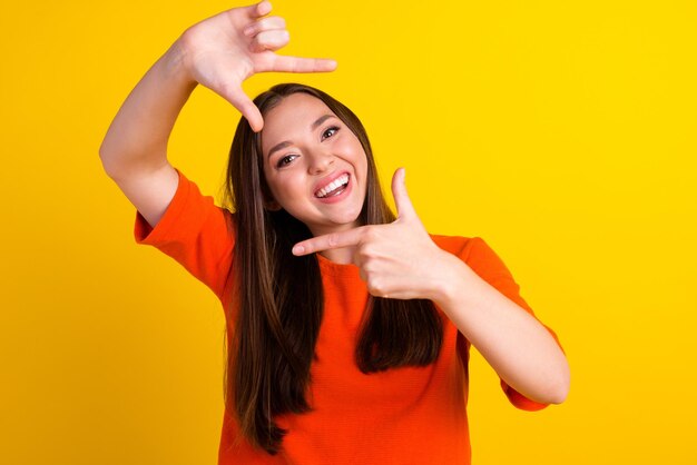 Young woman standing over yellow background doing frame using hands fingers camera perspective