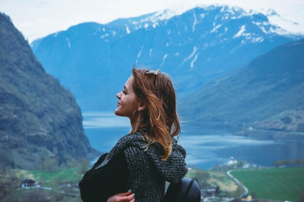 Young woman stands on the background of beautiful mountains and a lake, fjord flam Norway in spring season