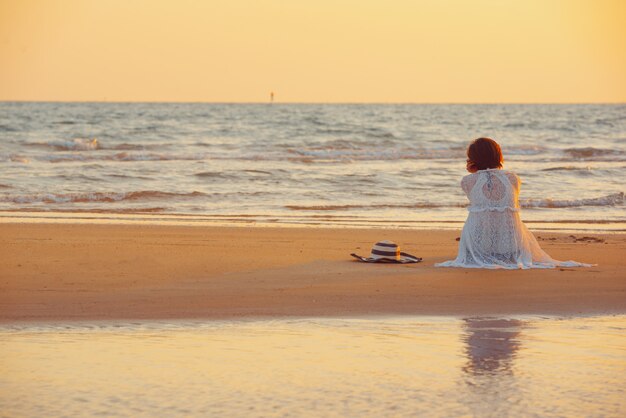 Una giovane donna si trova sulla spiaggia durante un tramonto, le vacanze estive.