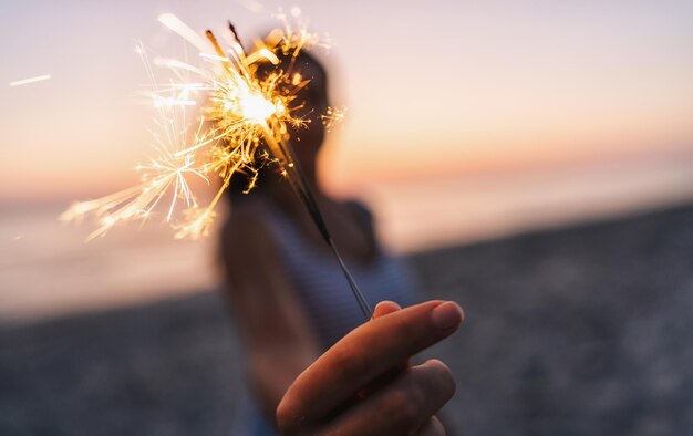 若い女性は夕日の光の中で線香花火とビーチに立っています