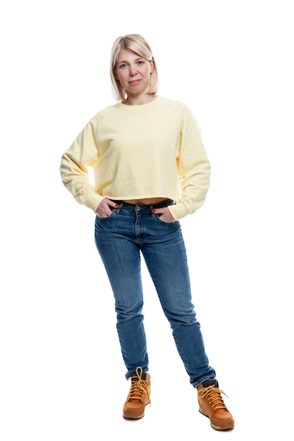 A young woman stands in full growth. Smiling blonde in a yellow sweater and jeans.