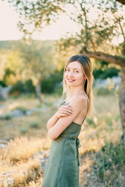 Young woman stands halfturned in the garden hugging her shoulders