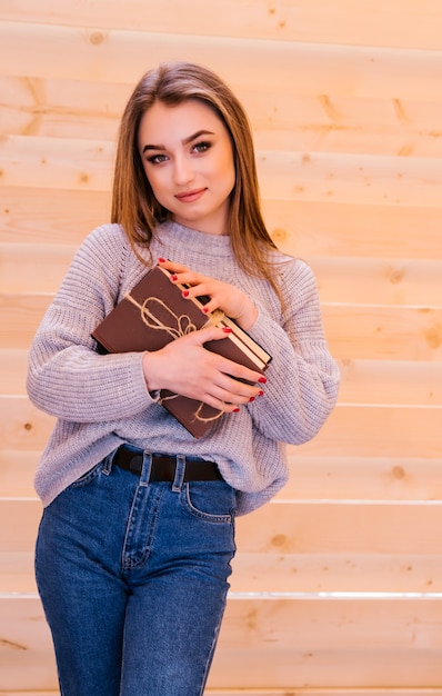 a young woman stands and holds a stack of books in her hands. books tied with string.