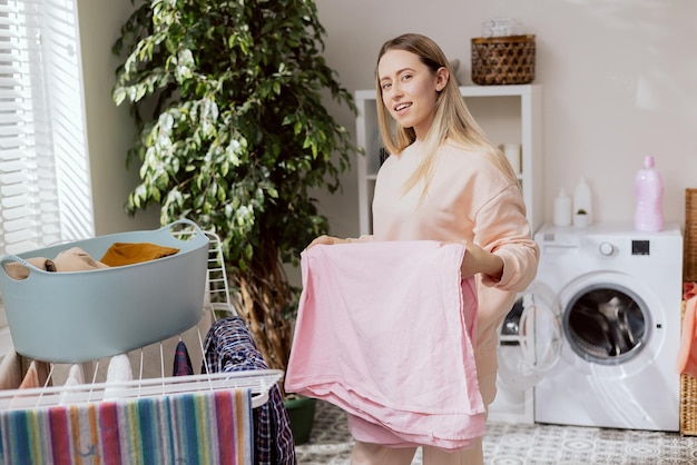 Young woman stands in laundry room by dryer and removes washed clean smelling clothes from bowl