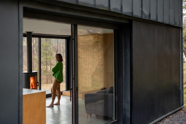 Young woman stands near fireplace at modern house on nature