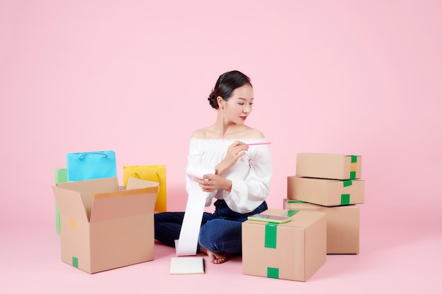 Young woman startup small business freelance sitting with parcel box mobile and sale receipt at home