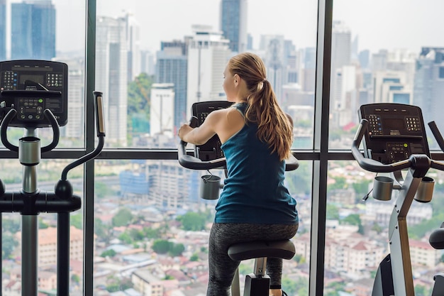 Young woman on a stationary bike in a gym on a big city background